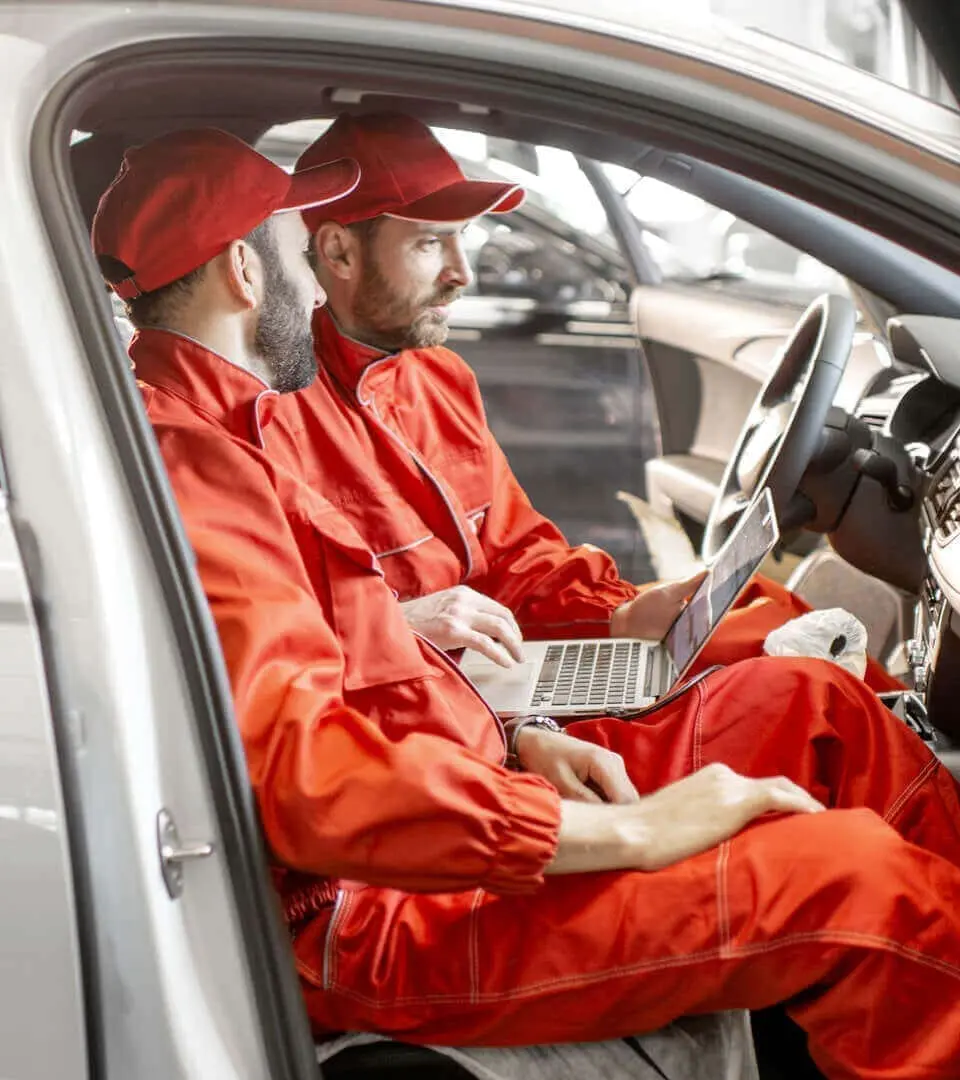 Two technicians in suits sitting in a car with a laptop