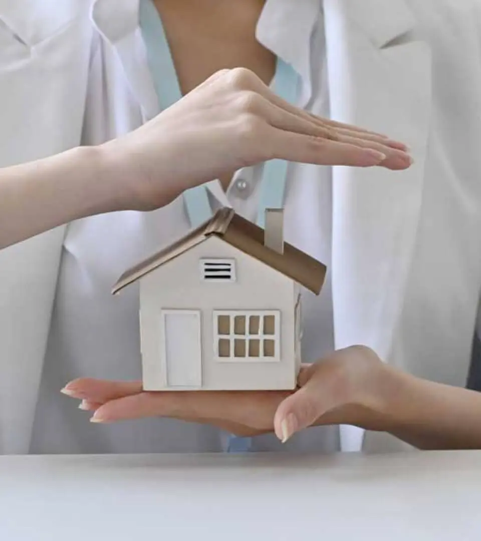 A woman holds a model house in one hand and protects it with the other