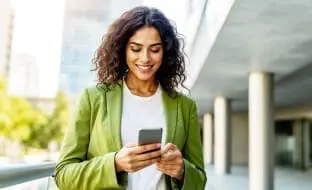 A smiling woman on the street uses her smartphone.