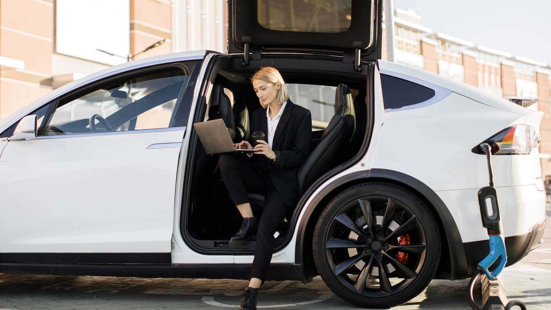 Donna con portatile seduta su un'auto sportiva con portiera ad ali di gabbiano aperta