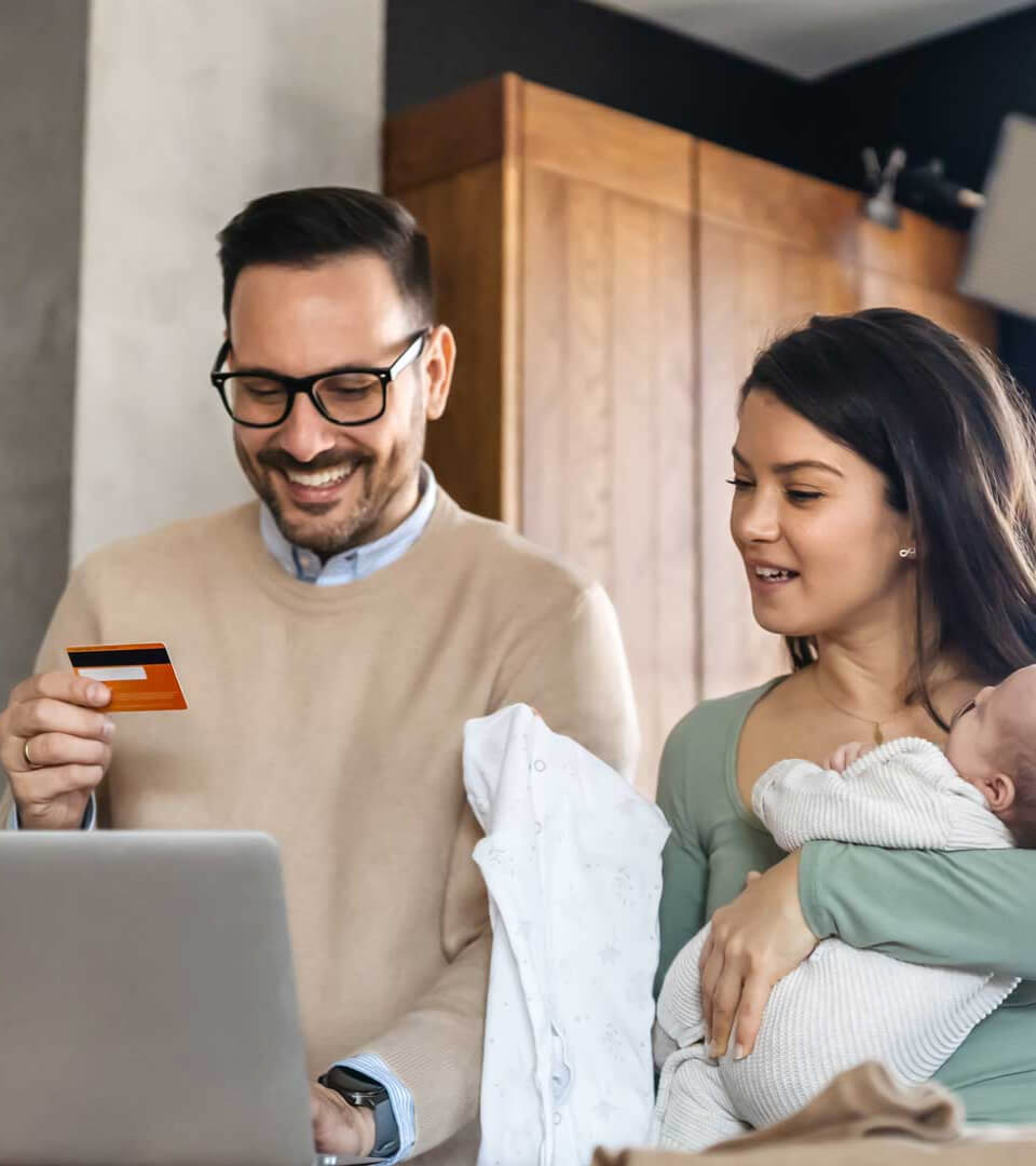 Coppia con neonato a casa davanti a un portatile con carta di credito