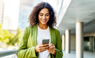 Una donna sorridente in strada usa lo smartphone.